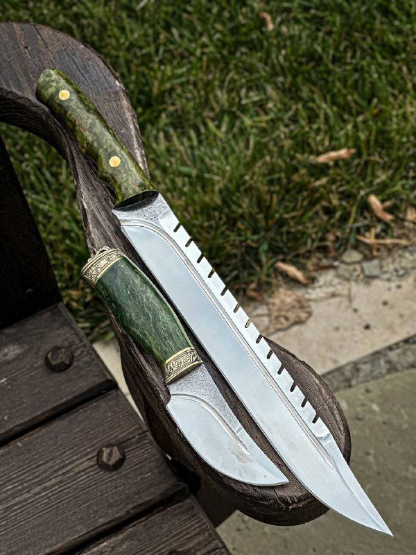 Крупный план одного цельнометаллического скотореза с зелёной стабилизированной рукоятью из карельской берёзы и отполированным длинным клинком, лежащего на ножнах.