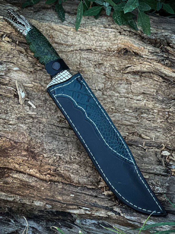 Фотография ножа «Крокодил» со вставленной кожаными ножнами: акцент на форму клинка, шов ножен и отделку рукояти.