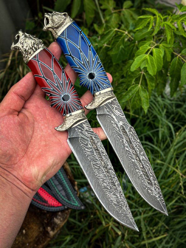 Два ножа на ладони с выразительными синими и красными акриловыми рукоятями, вид на клинки с видимым дамасковым узором и декоративными элементами.