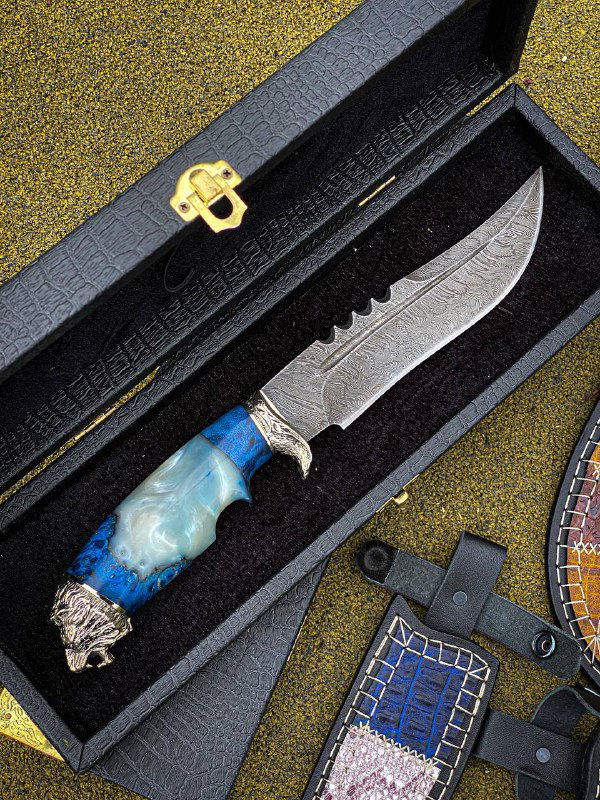 Крупный план ножа «Лев» с голубой/синей акриловой рукоятью, хорошо виден узор дамаска на лезвии и кусочек кожаной ножны.
