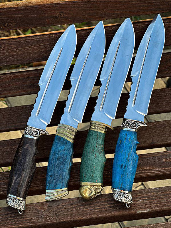 Четыре клинка рядом на деревянной поверхности, рукояти разного цвета, демонстрация одинаковой формы клинков и различных вариантов отделки рукояти.