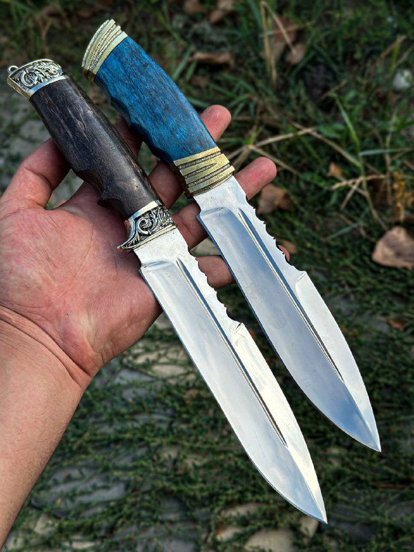 Два ножа в руке на фоне травы, вид на клинки и гаечки у рукоятей, показаны разные цветовые варианты и металлическая фурнитура.