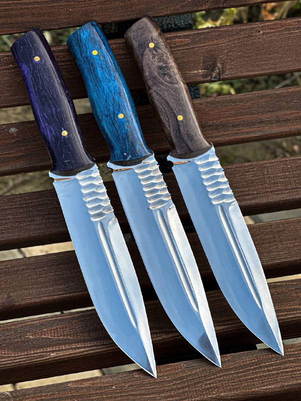 Четкий кадр трёх ножей на деревянной поверхности: зеркальная полировка клинков 95х18 и видимые мелкие детали конструкции ножа.