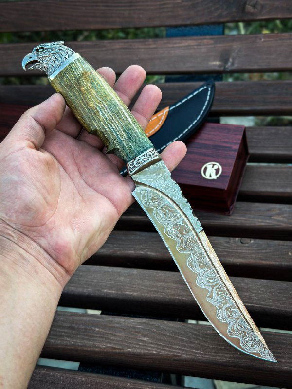 Нож в руке: крупный план рукояти из карельской берёзы и детальной гравировки дамаскового клинка с мельхиоровой гардой.