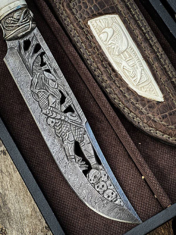 Детальный кадр клинка ножа «ВОИН»: сложная ручная резьба и вырезы по дамаску, хорошо видна текстура металла и художественная обработка в мастерской.