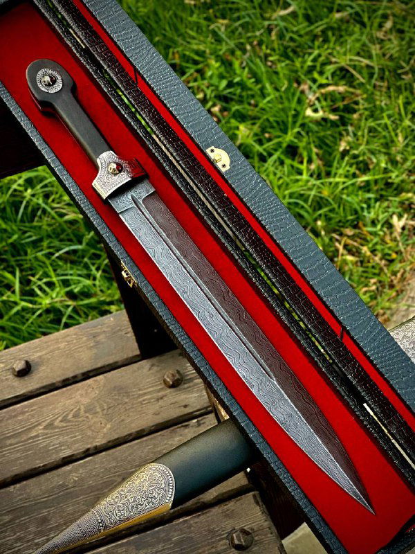 Открытый футляр с красной бархатной подкладкой и видимым клинком боевого кинжала; снимок сверху, скамейка и трава на фоне.