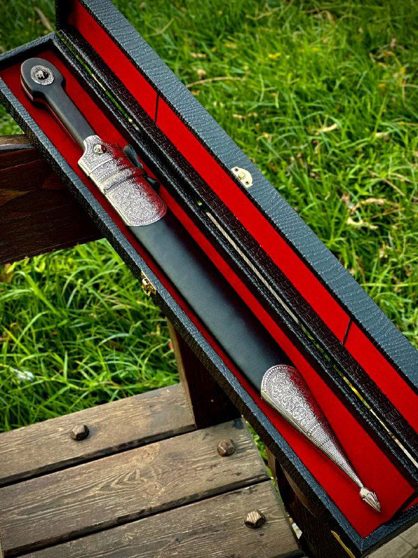 Внутренняя компоновка футляра: кинжал в ножнах с мельхиоровыми накладками, красная подкладка и часть скамейки на фоне.