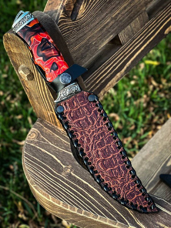 Нож в комплекте с кожаными ножнами: плетёный рисунок ножен, часть дамаскового клинка и акриловая рукоять видны на деревянном фоне.