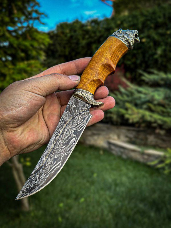 Нож «Лев» в руке мастера: детальный вид на рисунок дамаска, профиль рукояти из карельской берёзы и украшенные мельхиоровые гарды на торце.