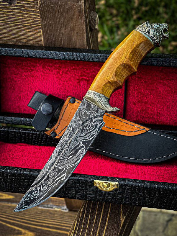 Фотография ножа «Лев» в футляре: дамасковый клинок, рукоять из карельской берёзы и кожаные ножны на фоне рабочего стола мастера.