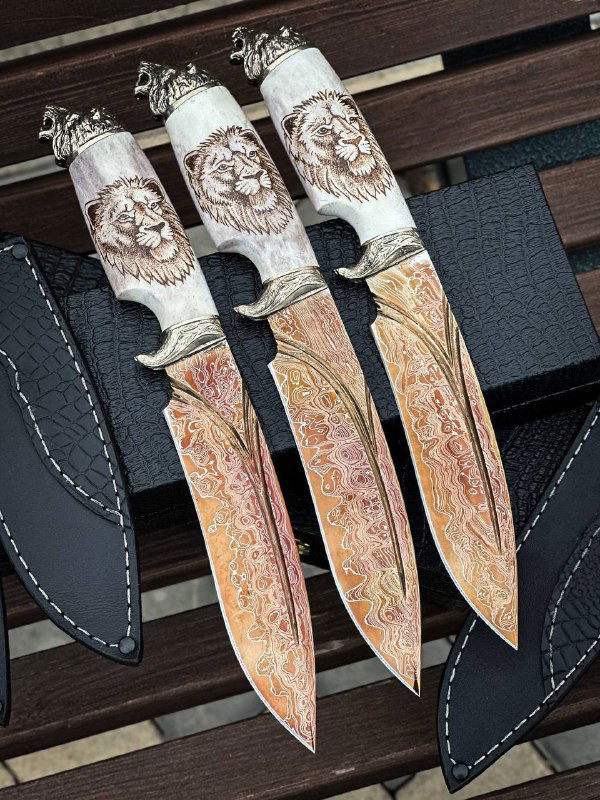 Три ножа «Лев» на фоне: выразительные узоры дамаска, окрашивание оксидом и оформленные рукояти из рога лося с изображением льва.