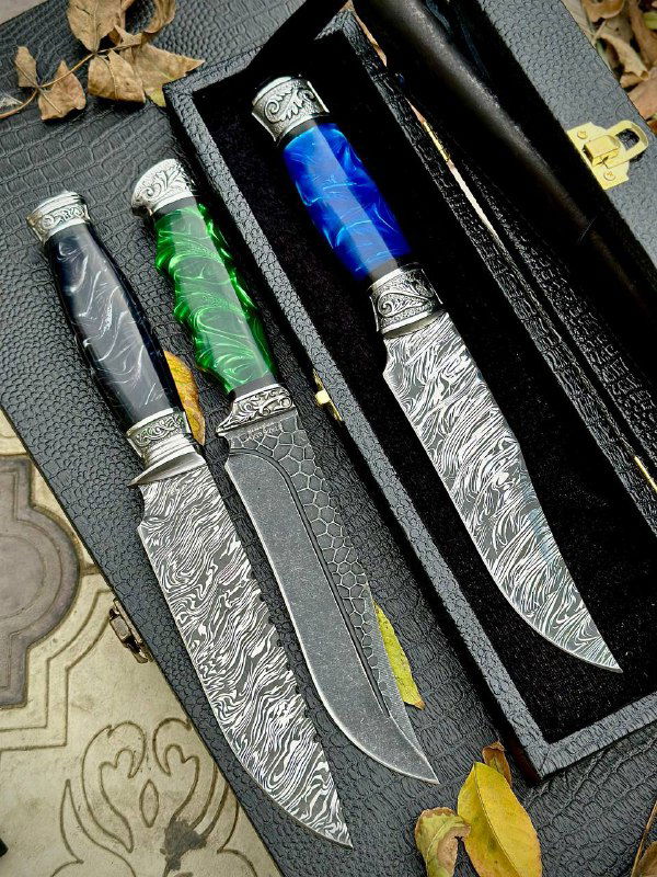 Три разделочных ножа в раскрытом виде в футляре: видны утопные кожаные ножны, разные формы клинков и акриловые рукояти разных цветов.
