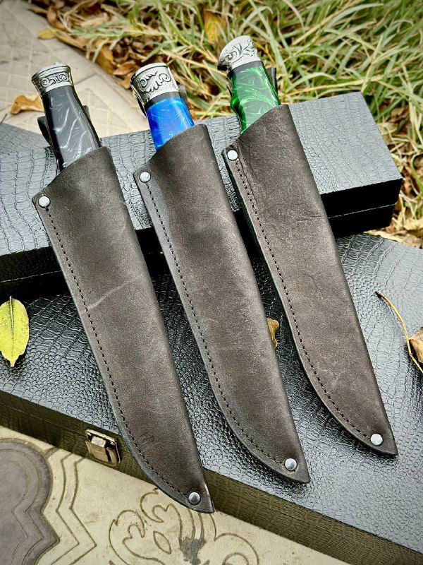 Утопные кожаные ножны трёх моделей на фоне травы и коробок: тёмная замша, швы и застёжки, подчёркивающие комплектность набора ножей.