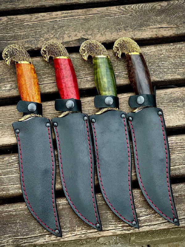 Четыре ножа «Орлан» в ножнах: кожаные ножны одного типа, оформление швов и форма клинков хорошо видны на фоне деревянной поверхности.