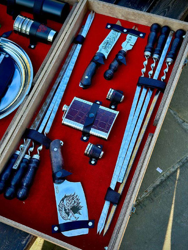 Детальный кадр набора: шампуры с деревянными ручками, ножи и точилка, уложенные в футляр-столик на лавке.