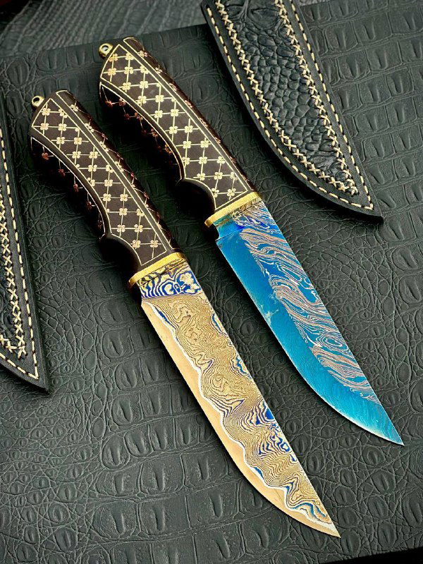 Пара ножей «Кобра» рядом с кожаными ножнами: видно рисунок дамаска, синее оксидирование и латунные гарды, крупный план.