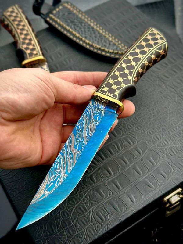 Крупный план синего дамаскированного клинка ножа «Кобра» в руке, видна рукоять из граба с геометрической инкрустацией.