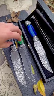 Рука держит один из ножей в наборе: видно текстуру клинка, форму кончика и отделку гарда, акцент на посадке рукояти в коробке.