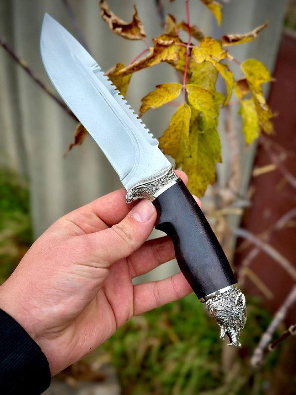 Нож «Волк» в руке под углом: видно форму клинка, переход к рукояти из граба и металлизированные элементы гарды и навершия.