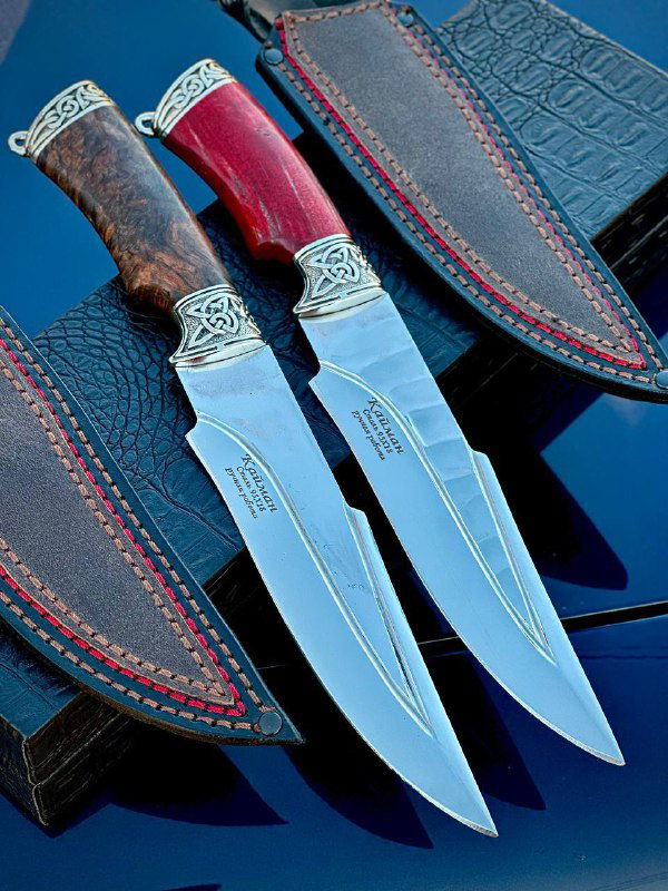 Три ножа рядом с кожаными ножнами: на изображении видны красные и тёмные акценты на рукоятях и строчка на ножнах.