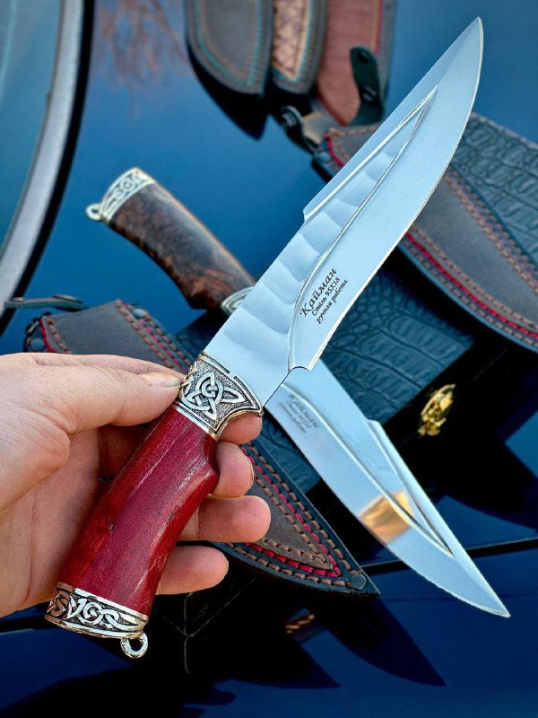 Рука показывает нож на фоне других экземпляров: видна полировка клинка, художественная гравировка и общая сборка изделия.