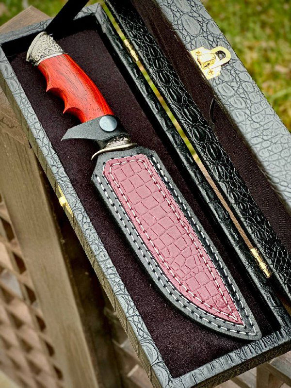 Нож «Тур» в кожаных ножнах внутри коробки: вид на ножны с красной вставкой, рукоять из падука и текстуру дамаска на клинке.