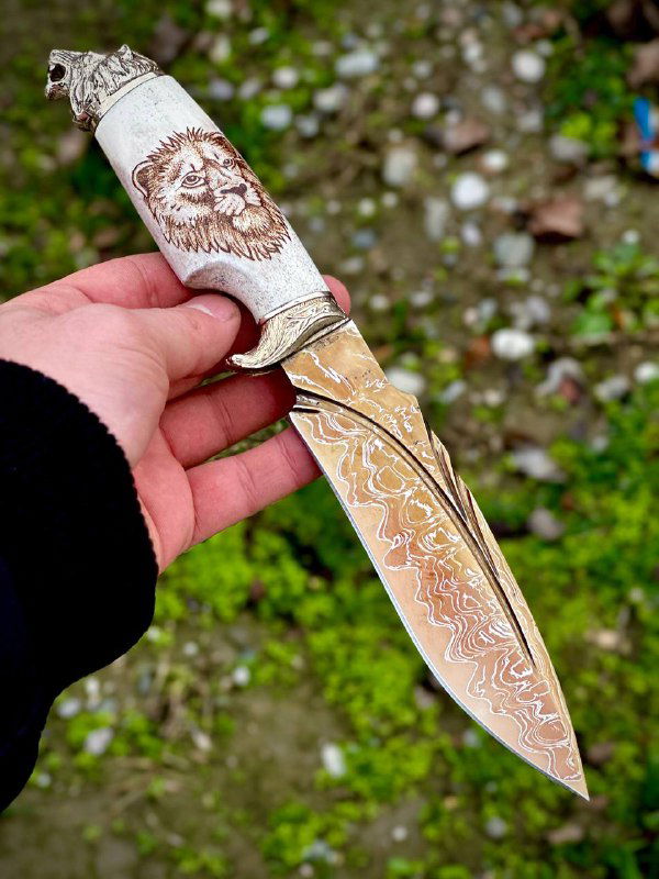 Рука держит один нож: крупный план дамасковой поверхности клинка с выгравированными узорами и резной рукоятью из рога.