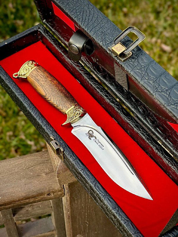 Фото ножа «Скорпион» в футляре крупным планом: декоративные латунные гарды, текстура рукояти из ореха и красная внутренняя отделка футляра, вид сбоку.