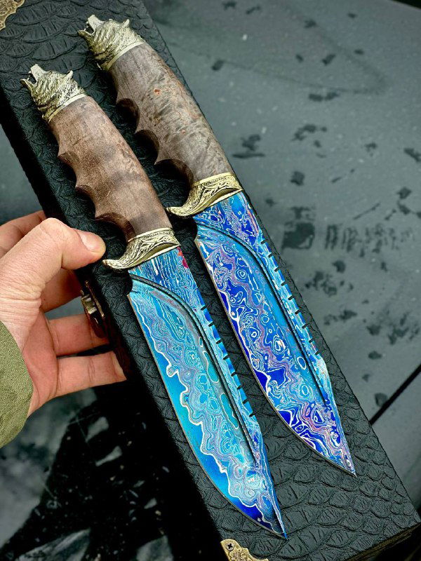 Два ножа с эффектным синевато-ярким рисунком на лезвиях; видны рукояти из стабилизированной древесины и декоративные гарды металлического цвета.