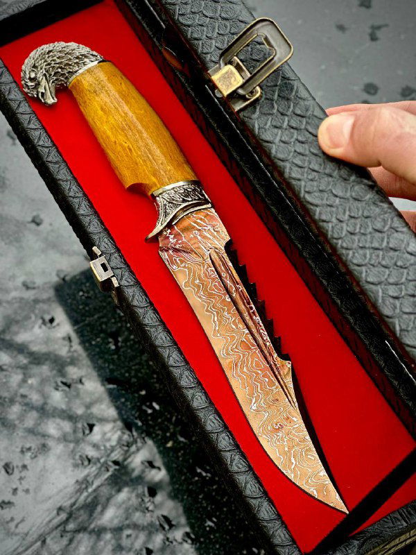 Нож в открытом подарочном футляре с красным бархатным вкладышем; видны декоративные металлические элементы и кожаные ножны рядом с изделием.