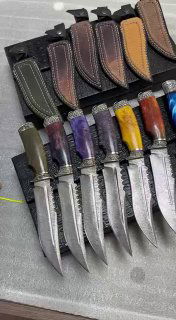 Фотография нескольких ножей крупным планом: видны текстуры дамаска на лезвиях и яркие полупрозрачные рукояти, выложенные в ряд.