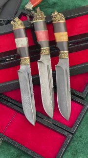 Вид трёх ножей с дамасковой стали на зелёном фоне; видна текстура клинков и сочетание рукоятей из берёзы и чёрного граба.