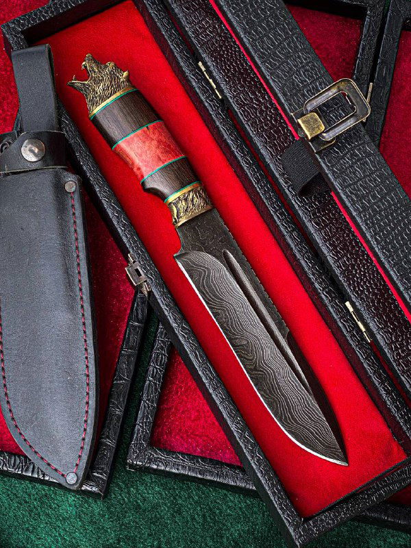 Нож в чёрных кожаных ножнах, размещённый в футляре с красным бархатным вкладышем; видна латунная гарда и форма клинка.