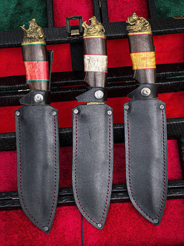 Три ножа в чёрных кожаных ножнах, расположенные рядом, показаны лицевые стороны клинков и аккуратная строчка на ножнах.