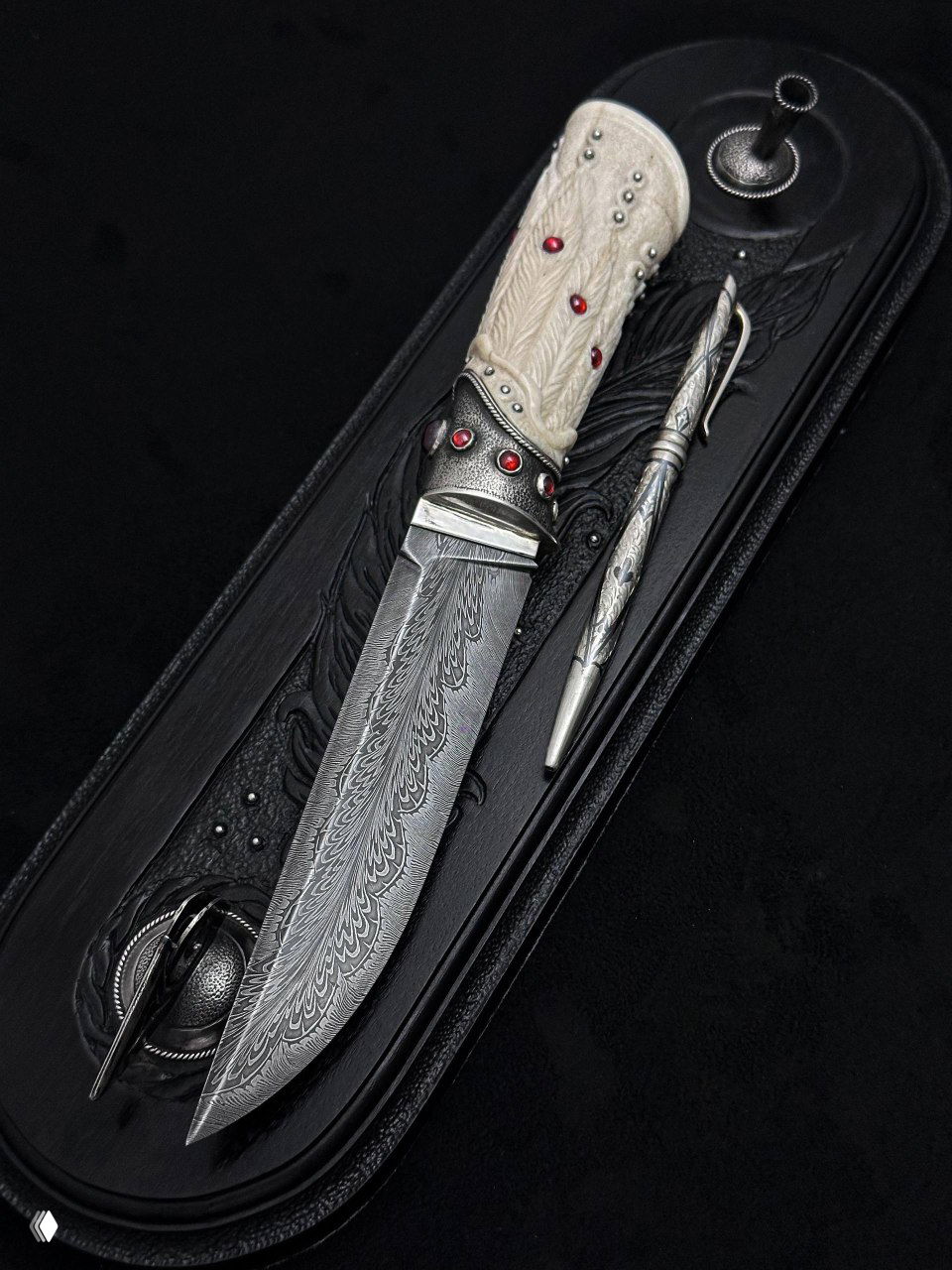 Крупный план ножа под углом: видно узор мозаичного дамаска на лезвии и украшения из серебра у рукояти на тёмной текстуре.