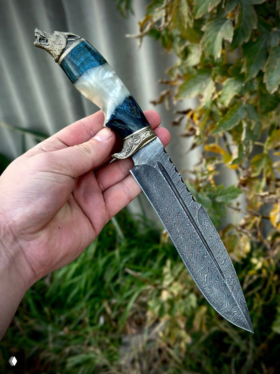 Один нож в руке: вид на длинный дамасский клинок и комбинированную рукоять с белыми и синими вставками из акрила и карельской берёзы