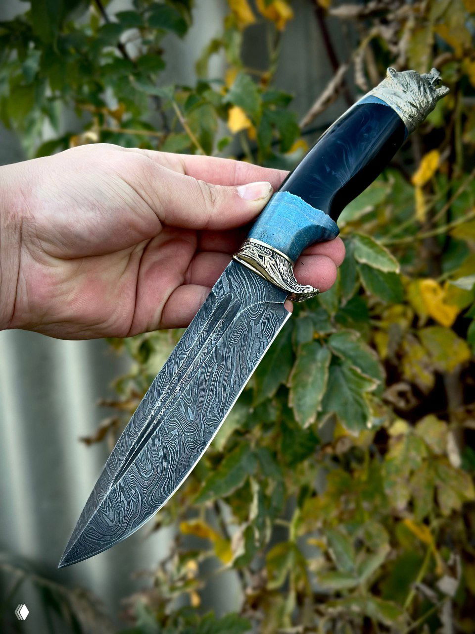 Крупный план острия дамасского клинка в руке мастера — видна текстура металла, профиль лезвия и поперечная насечка возле гарды