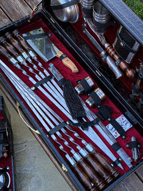 Крупный план внутренней панели кейса: ровно разложенные шампуры, ножи с деревянными рукоятками, точилка и другие принадлежности для шашлыка.