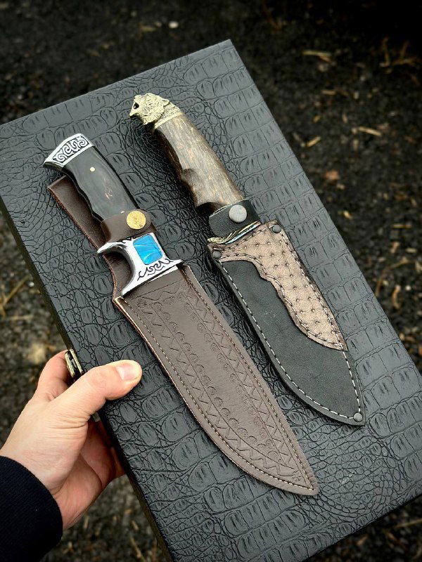 Два ножа в кожаных ножнах на чёрной подложке, крупный план рукоятей — видна текстура карельской берёзы и мельхиоровые гарды.