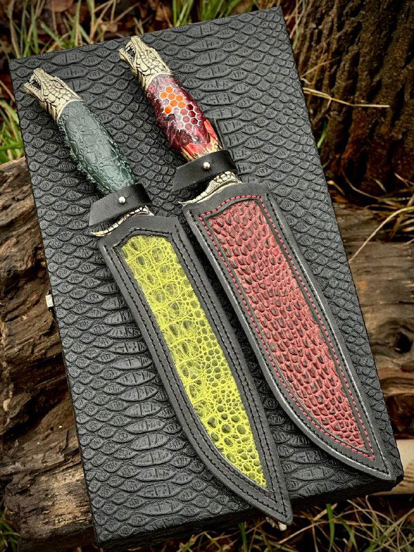 Две кожаные ножны с вставками зелёного и красного рисунка рядом с кинжалами «Дракон» на текстурированном фоне — комплект к ножам.