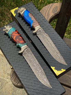 Вид сверху: два дамасковых клинка с разноцветными рукоятями (синий и мраморный), чёрные тиснёные коробки и детали мельхиоровых гард.