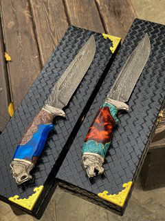 Пара ножей раскрыта в коробках на деревянной лавке; видно текстуру дамасской стали на лезвиях и сочетание карельской берёзы с акрилом на рукоятях.