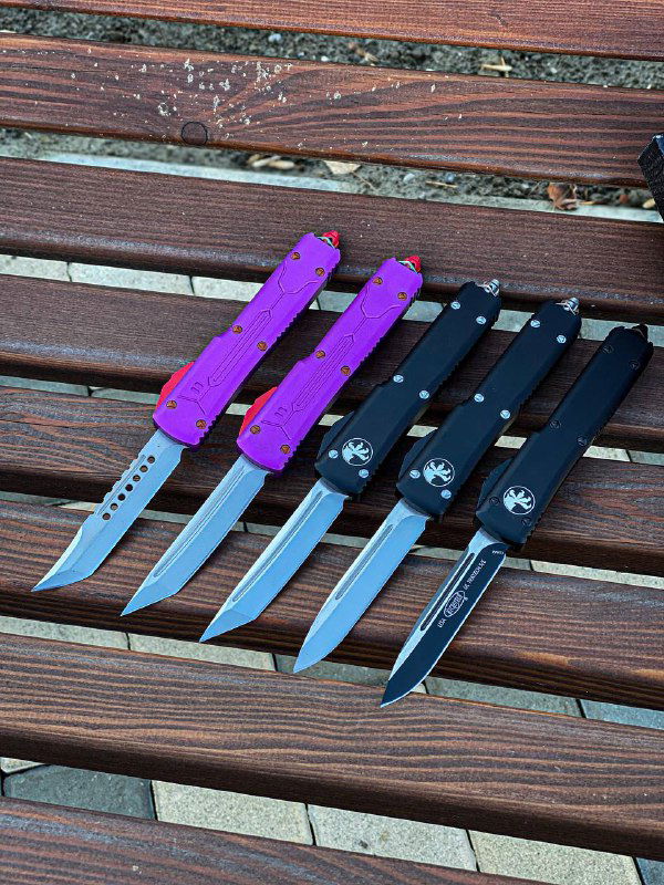 Ряд автоматических ножей Microtech с фиолетовыми и чёрными рукоятями положен на деревянную поверхность, вид сверху показывает рукояти и клинки.