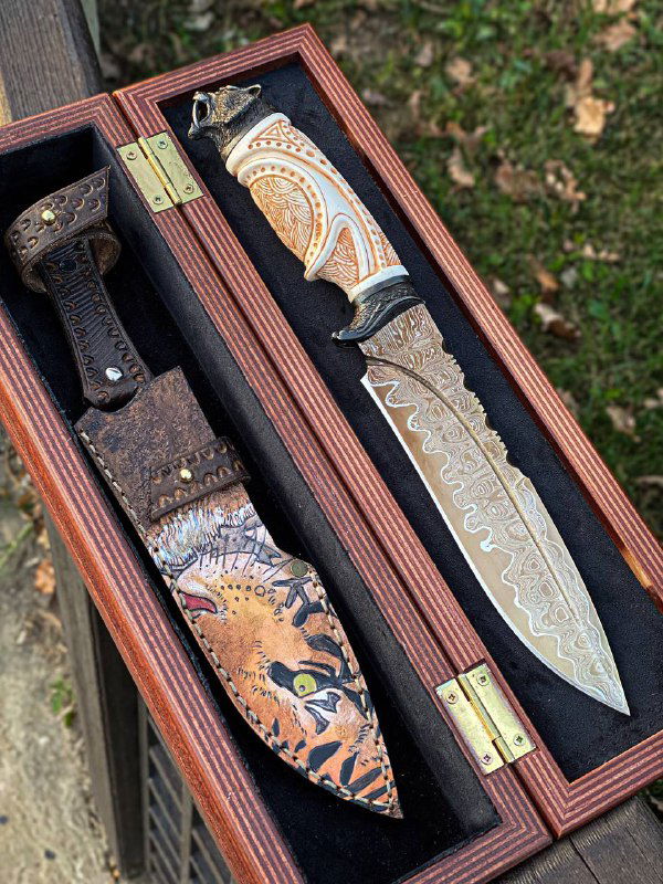 Крупный план клинка и ножен: заметна текстура дамасской стали, узор на кромке и декоративное оформление ножен с тигровым мотивом.