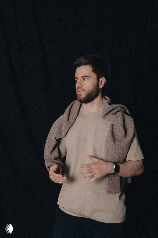 Мужчина в светлой одежде жестикулирует на тёмном фоне во время выступления — спикер или лектор, визуальный образ рассказа о работе с инфобизнесом.