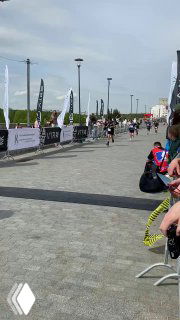 Финишная прямая Зеленоградского полумарафона: бегуны на дистанции 10 км, флаги и ограждения вдоль трассы, зрители у барьера.