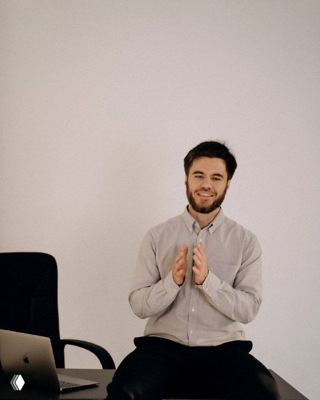 Мужчина в светлой рубашке сидит на стуле и улыбается, похлопывая в ладоши на нейтральном фоне — иллюстрация для поста об ИИ и трафике.