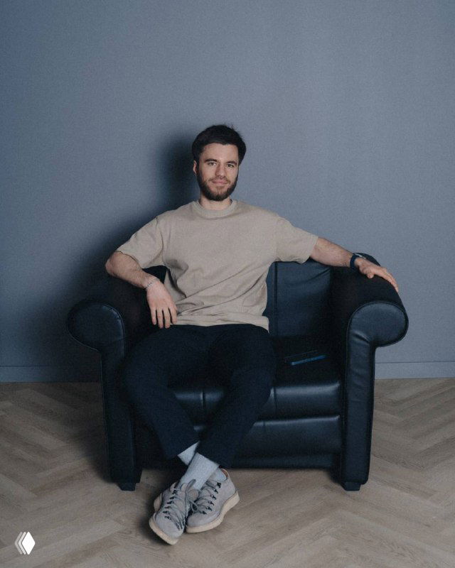 Мужчина в повседневной одежде сидит в кресле на фоне серой стены; фотография иллюстрирует пост о рекламе, трафике и воронке продаж.