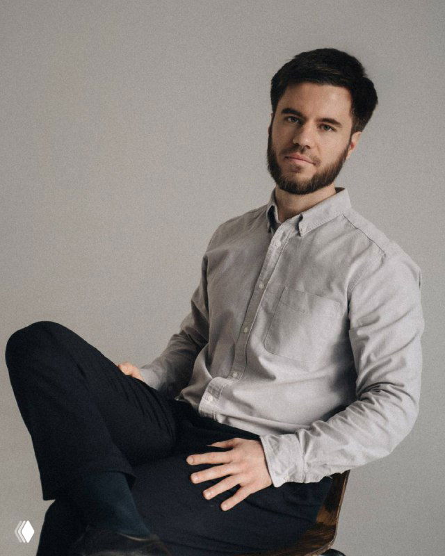 Портрет мужчины в светлой рубашке, сидит на стуле на нейтральном фоне; деловой спокойный образ, иллюстрация для поста о закрепе в Telegram.