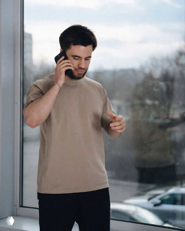 Фотография человека в повседневной одежде, говорящего по телефону у окна в офисном или жилом интерьере — иллюстрация деловой беседы о рекламе и договоре.